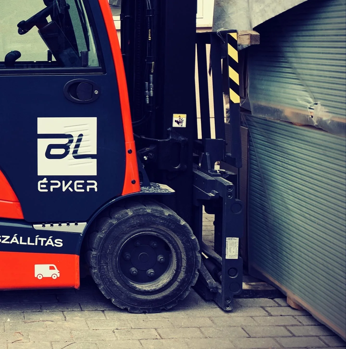 BL Épker targonca BL ÉPKER vállalati logó részlet – fehér plottervágott logó és kék SZÁLLÍTÁS felirat a piros karosszérián