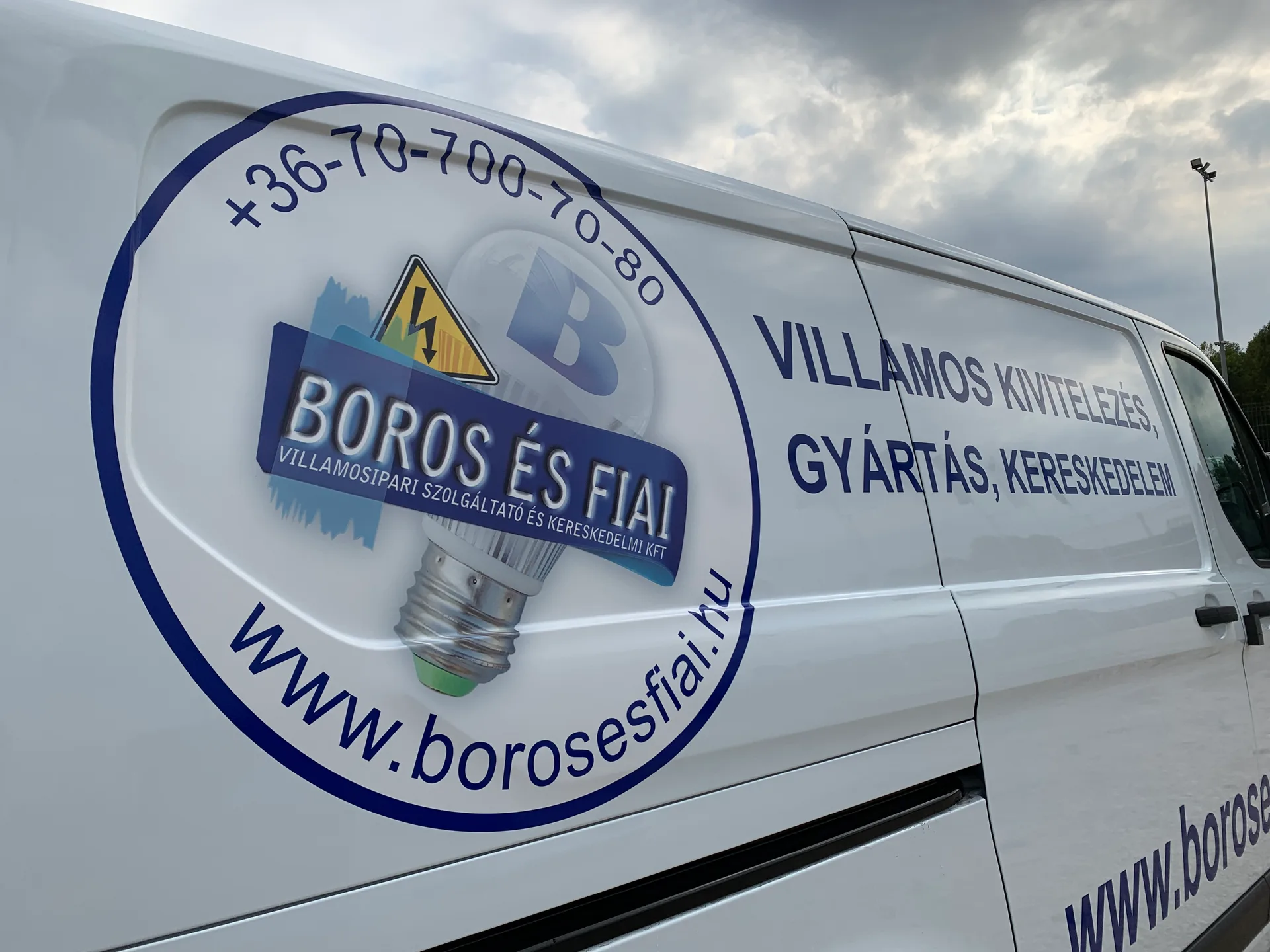 Boros és Fiai Ford Transit Custom oldal-dekor részlet – kerek vállalati logó villamosipari szimbólumokkal és szolgáltatási feliratokkal a jármű oldalfalán