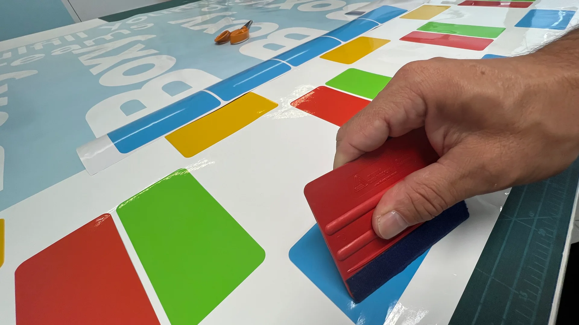 Betűvágott Boxy fólia kigyomlálása és applikálása – piros simítólappal történő rögzítés, színes geometrikus formák készre dolgozva