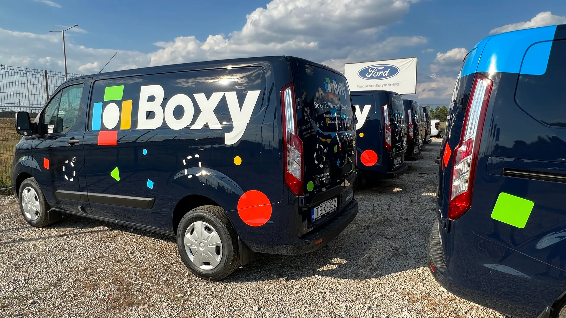 Boxy Ford Transit Custom flotta részlet – két jármű egységes oldal- és hátsó dekorral a FordStore Solymár-M3 háttérrel