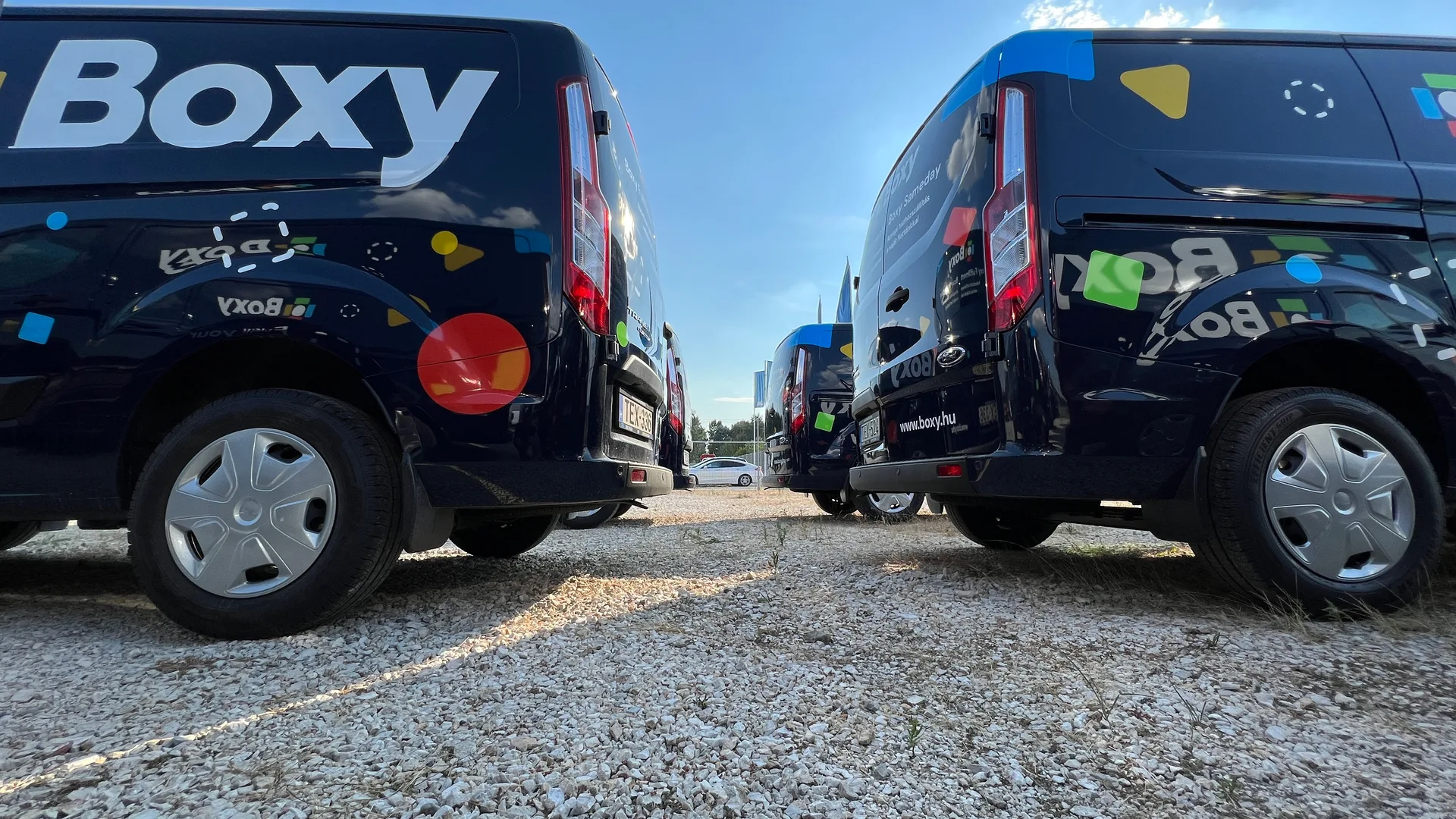 Boxy Transit Custom flotta alulnézetből – két sötétkék jármű hátsó dekorral, Boxy logó és színes formák drámai égbolt alatt