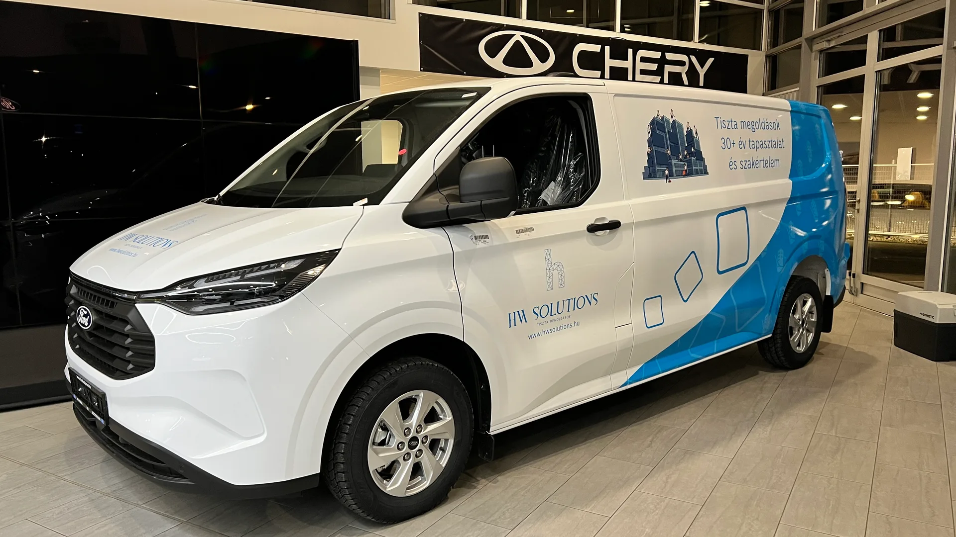 HW Solutions Ford Transit Custom – fehér karosszérián HW Solutions logó és kék hullámos vezérgrafika a hátsó harmadban, épülettisztításra utaló illusztrációval