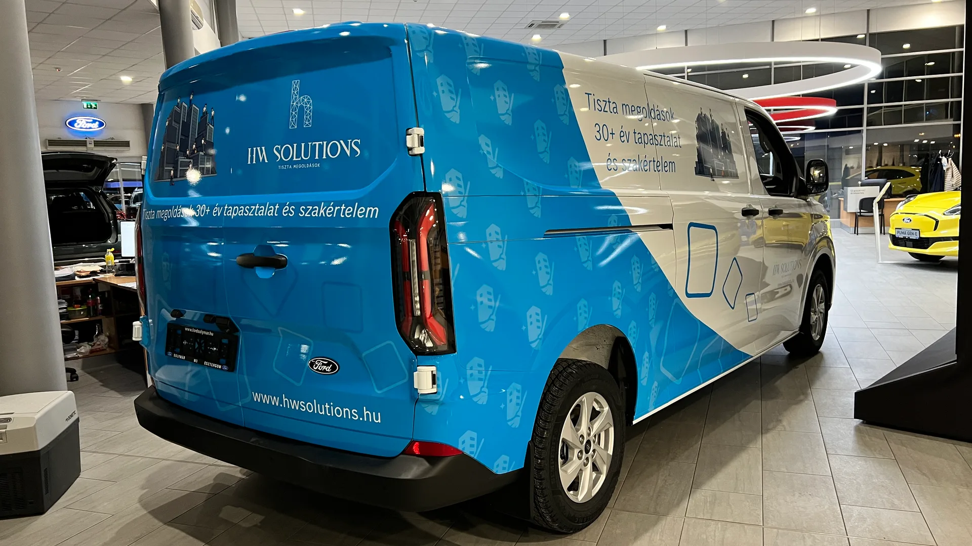HW Solutions Ford Transit Custom járműdekoráció jobb hátsó 3/4 nézet – a kék arculati elemek folytonosan futnak át a hátsó ajtóra, kiegészülve a HW Solutions logóval és weboldallal