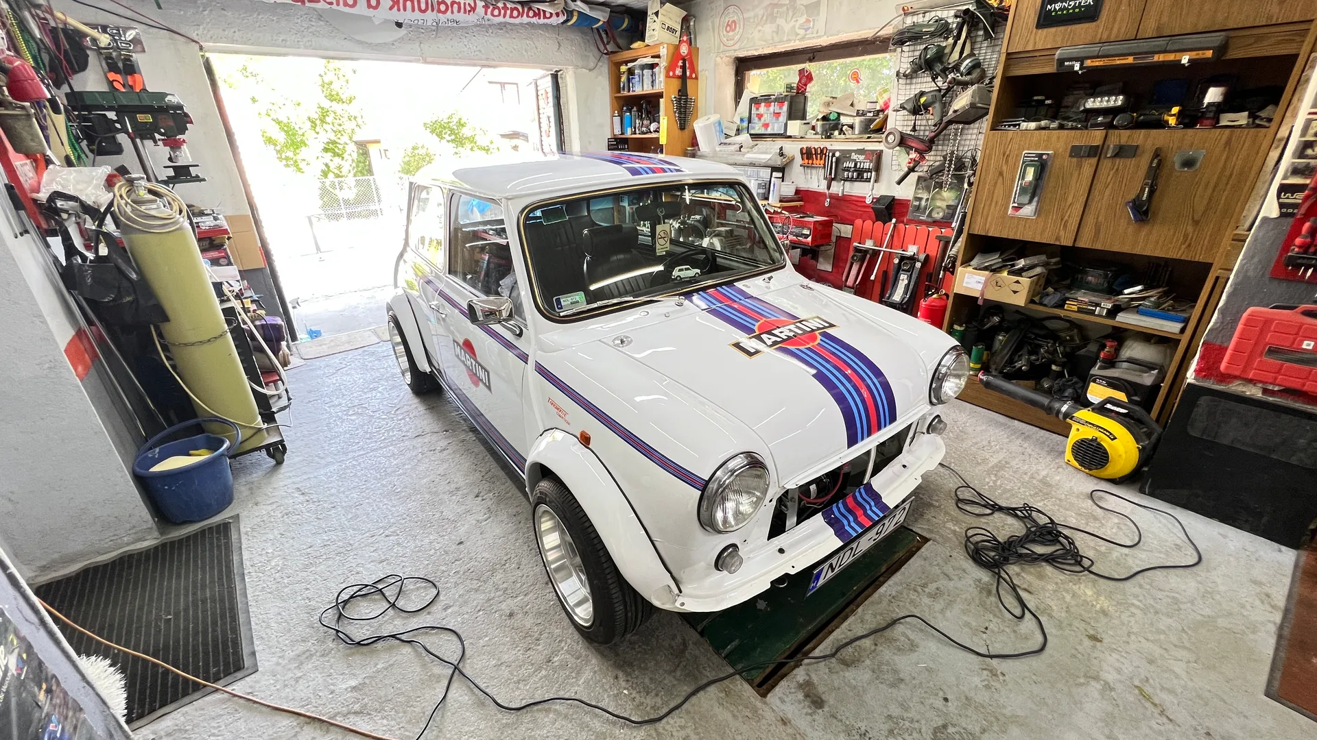 Elkészült Martini Racing dekoros klasszikus Mini háromnegyedes nézetből egy restaurátorműhelyben, a teljes csíkrendszerrel és motorháztető-grafikával