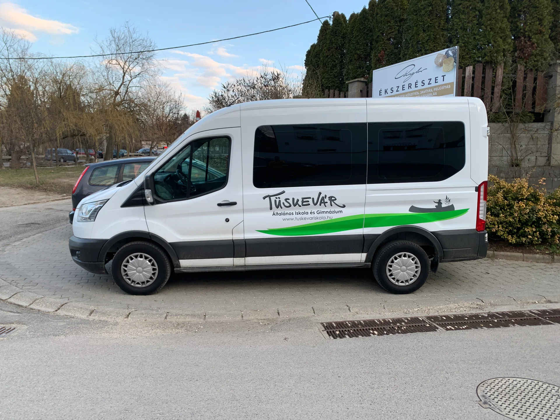 Oldalnézeti fotó a Tüskevár Általános Iskola és Gimnázium fehér Ford Transit szállítóbuszáról, zöld-szürke vágott dekorációval